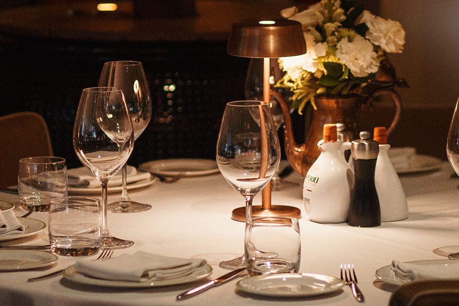 Table set for dinner with wine glasses and a copper lamp